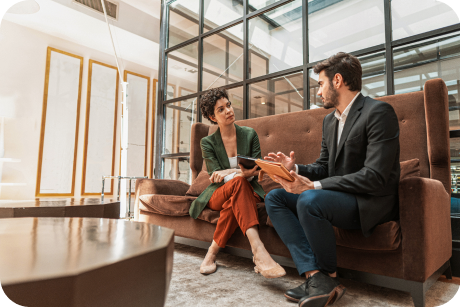 Two people sit on a couch discussing work.