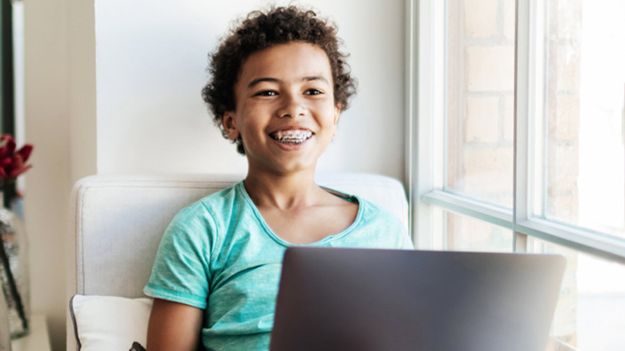 Child in teal shirt smiling while looking at a laptop