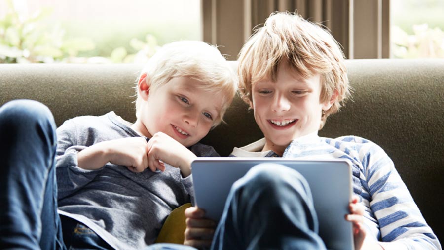 Two kids on couch smiling looking at a tablet