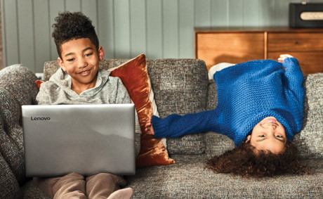 Two kids on a couch laying down and using a laptop