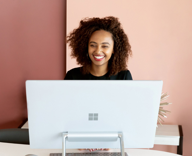 A smiling woman sits behind a Microsoft-branded computer