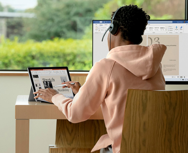 Young person using headsets working in front of the laptop and desktop computer.