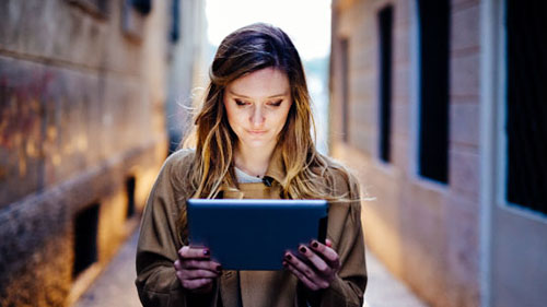 A woman holding a glowing tablet in an alley