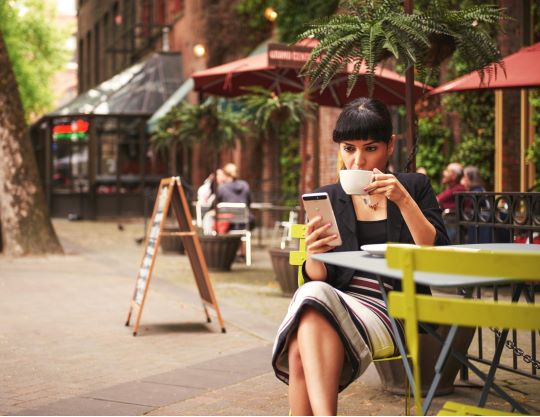 A woman drinking a cup of coffee at a table outside