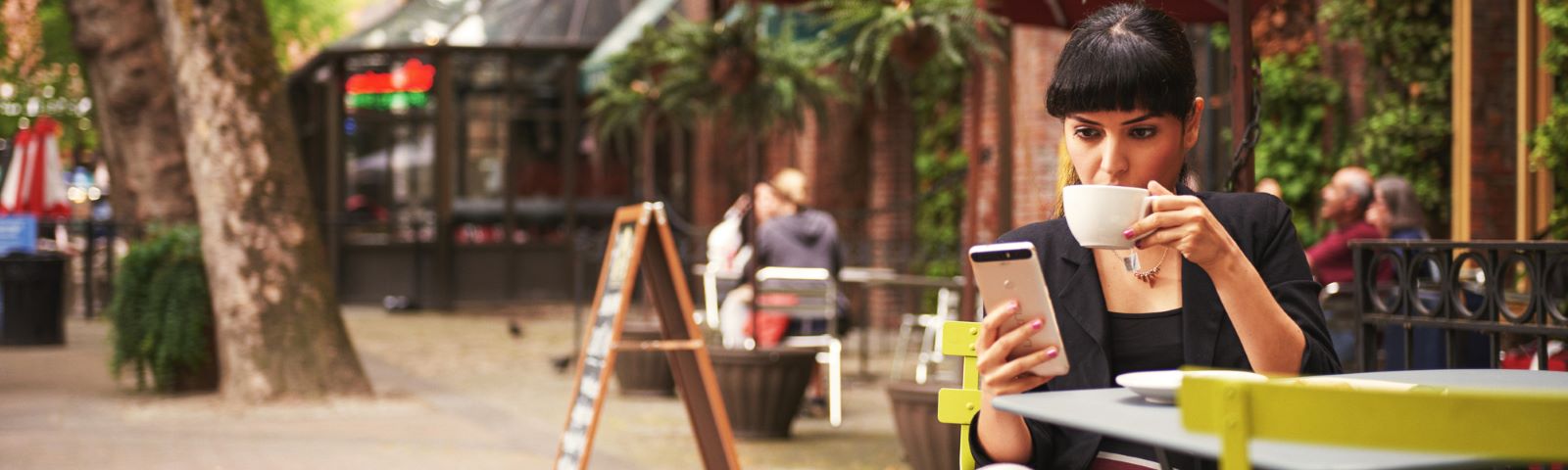 A woman drinking a cup of coffee at a table outside