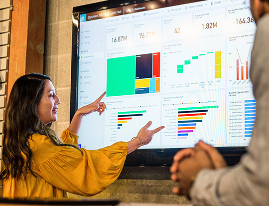 Woman in a yellow top explaining the graphs displayed on a large screen