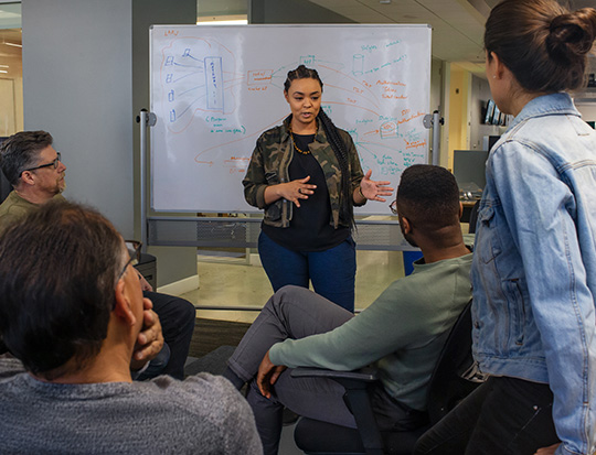 A woman with black hair giving a presentation to her colleagues