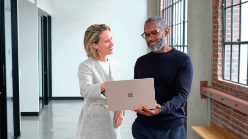 Man and woman standing in an office hallway discussing content on a laptop