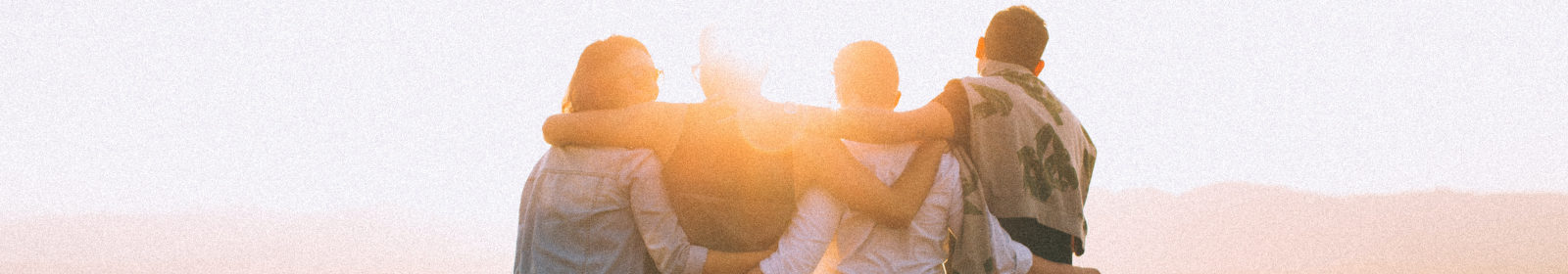 people are standing on a hill arm in arm watching the sunset