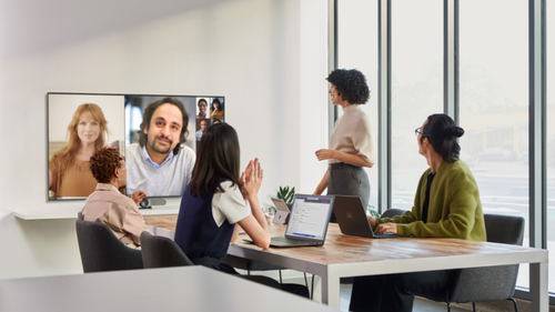 Four people around a boardroom table joined by virtual guests on a large screen