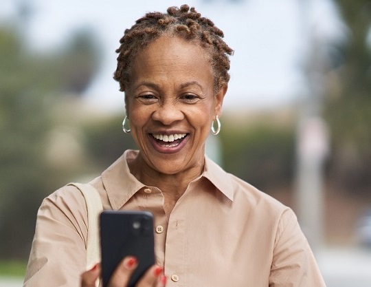 A woman is looking at her phone and smiling while walking outside