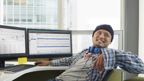 A developer smiling at his desk in front of multiple monitors