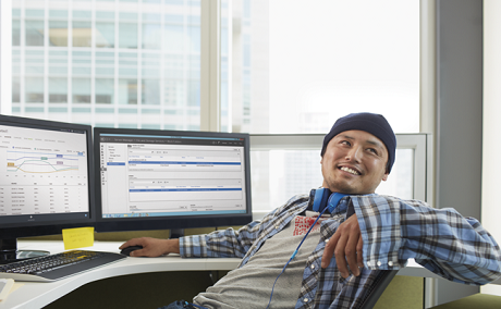 A developer smiling at his desk in front of two computer monitors