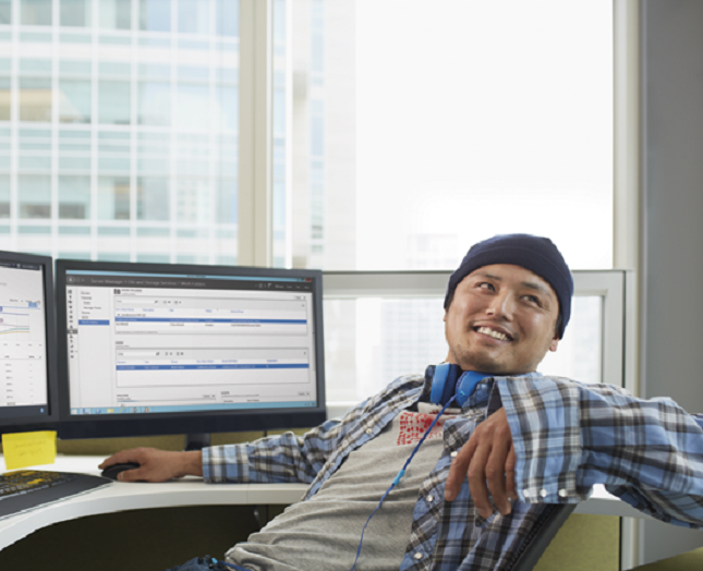 A developer smiling at his desk in front of two computer monitors