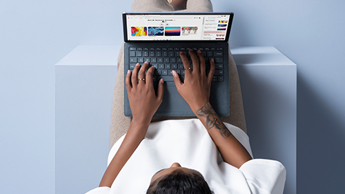 The photo shows a woman sitting with the laptop on her lap.