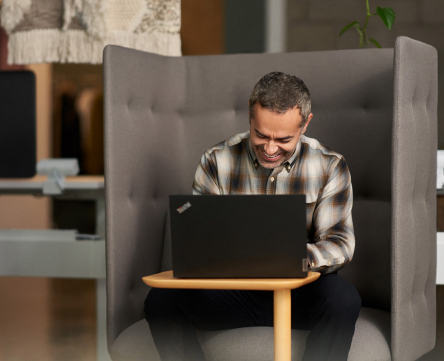 A laughing man in front of his laptop in a private booth