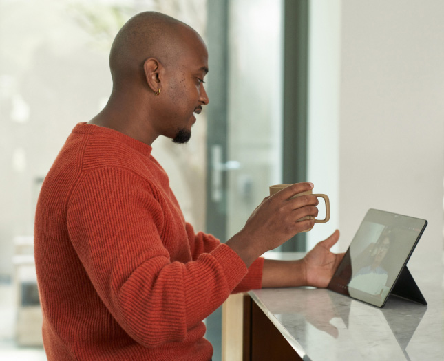 A man holding a cup in his hand while having a video call on his tablet