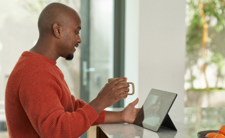 A man holding a cup in his hand while having a video call on his tablet