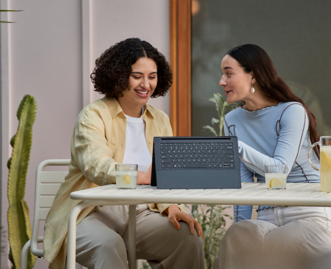 Two smiling women having lemonades in front of a laptop