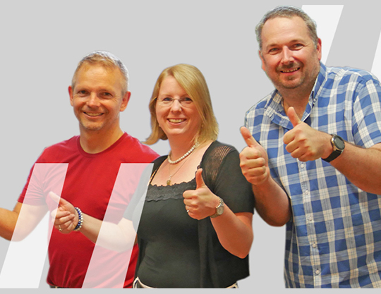 Zu sehen sind zwei Männer und eine Frau die mit erhobene Daumen in die Kamera lächeln.