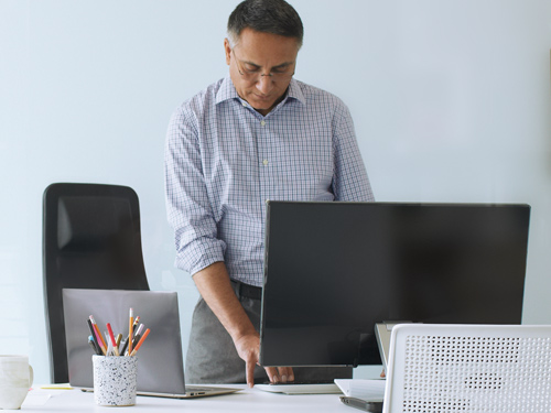 Man standing at desk with desktop and Surface laptop