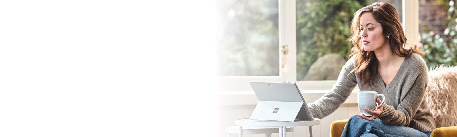 Person holding a mug in one hand and typing on a laptop