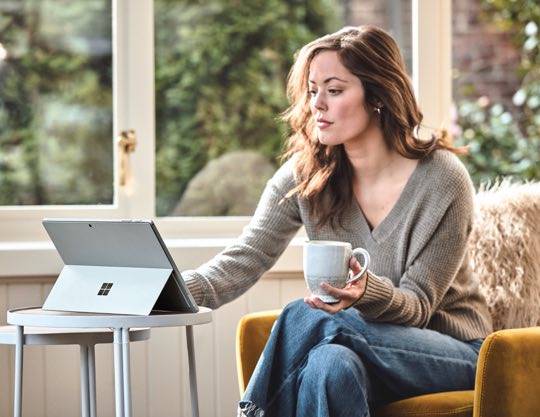 Person holding a mug in one hand and typing on a laptop
