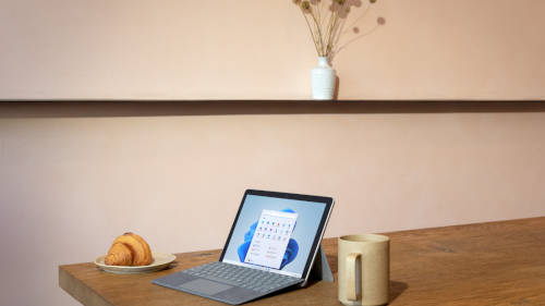 Ein Surface Laptop auf einem Tisch. Rechts davon ein Croissant und links daneben eine Kaffeetasse.