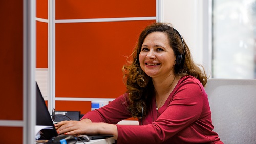 A smiling woman wearing a headset using her laptop