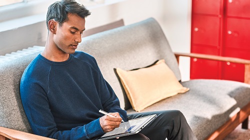 A man sitting on a sofa writing with a stylus on a tablet