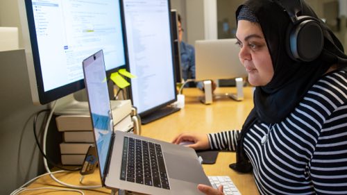 Person wearing headphones at a desk working on a laptop