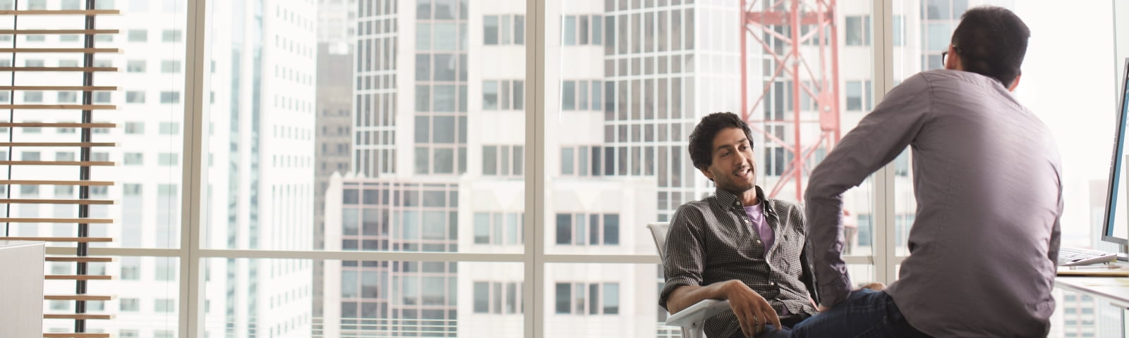 Two men talk with a cityscape behind them