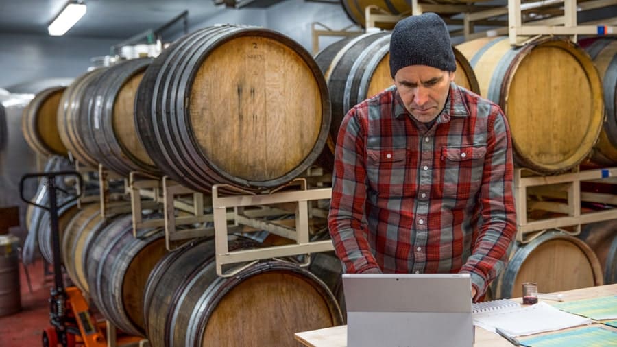 Man working on device in front of wooden barrels