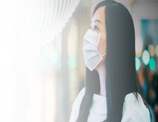 Woman in surgical mask stands looking at Stock ticker