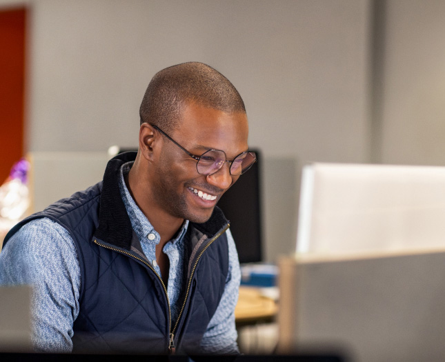 A person in casual clothing laughs while looking at a computer monitor