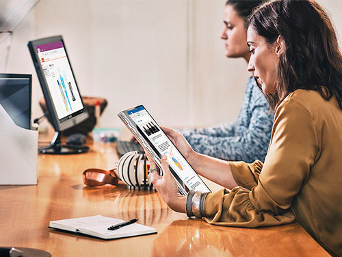 Two colleagues working on a tablet and desktop computer