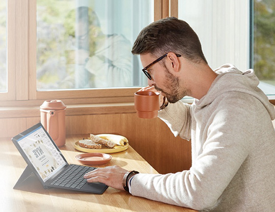 Person works on computer over breakfast in a sunny room