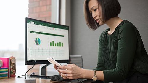 Woman looks at phone next to computer