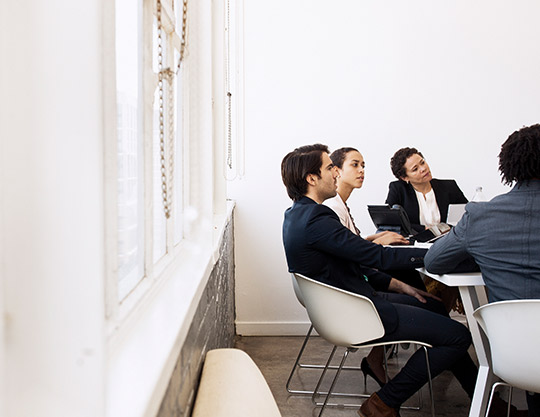 4 coworkers sitting near window having a meeting 