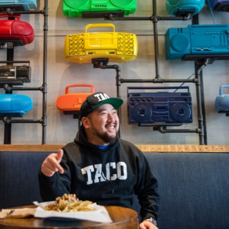 Man sitting in a booth smiling and pointing to a plate of Mexican food