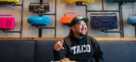 Man sitting in a booth smiling and pointing to a plate of Mexican food