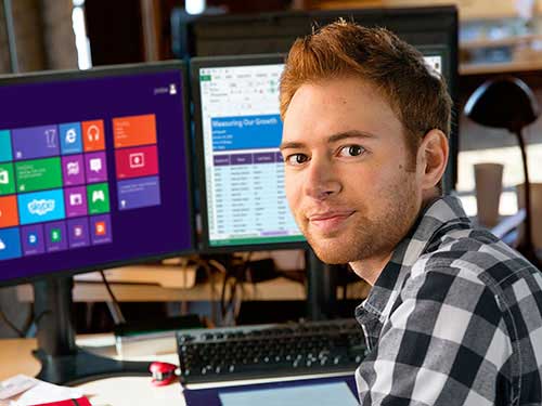 Image of man posing for photo in front of desktop computers 