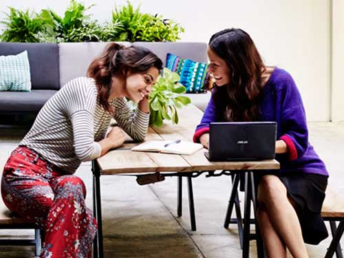 Image of two females working outside on laptop computer 