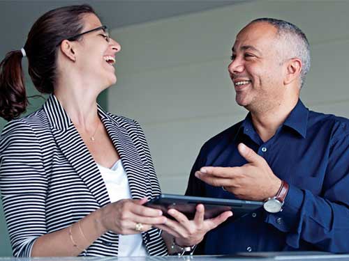 Two coworkers laughing while working on tablet 