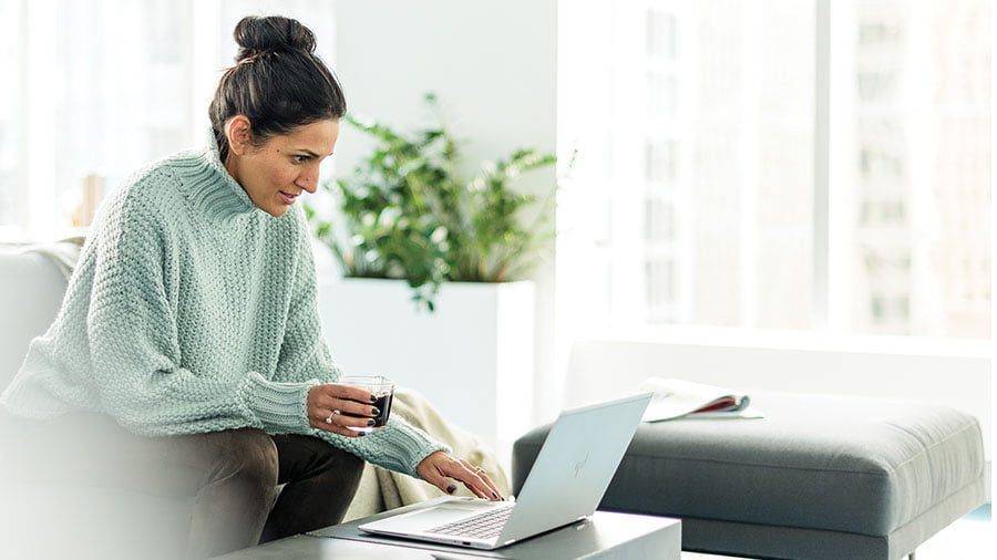 Woman holding a glass working on Surface laptop from home