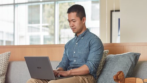 Person sitting on a couch smiling working on a laptop