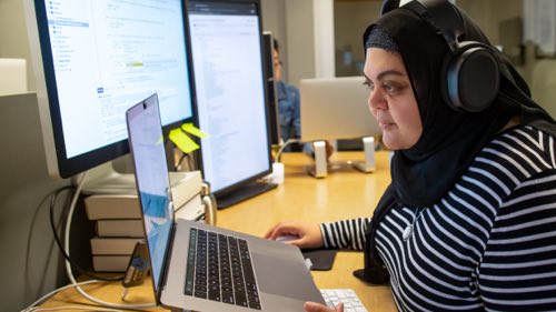 Person wearing headphones at a desk working on a laptop