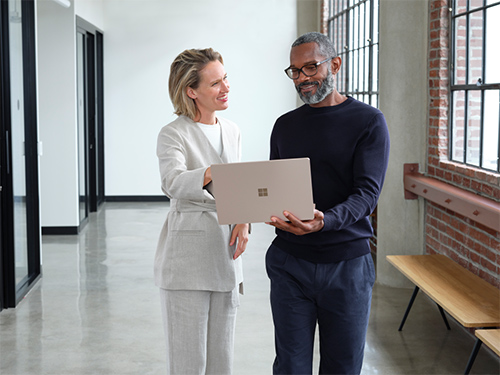 Two colleagues chatting in the hallway, one holding a Surface device