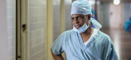 A doctor wearing scrubs, a head covering, and face mask