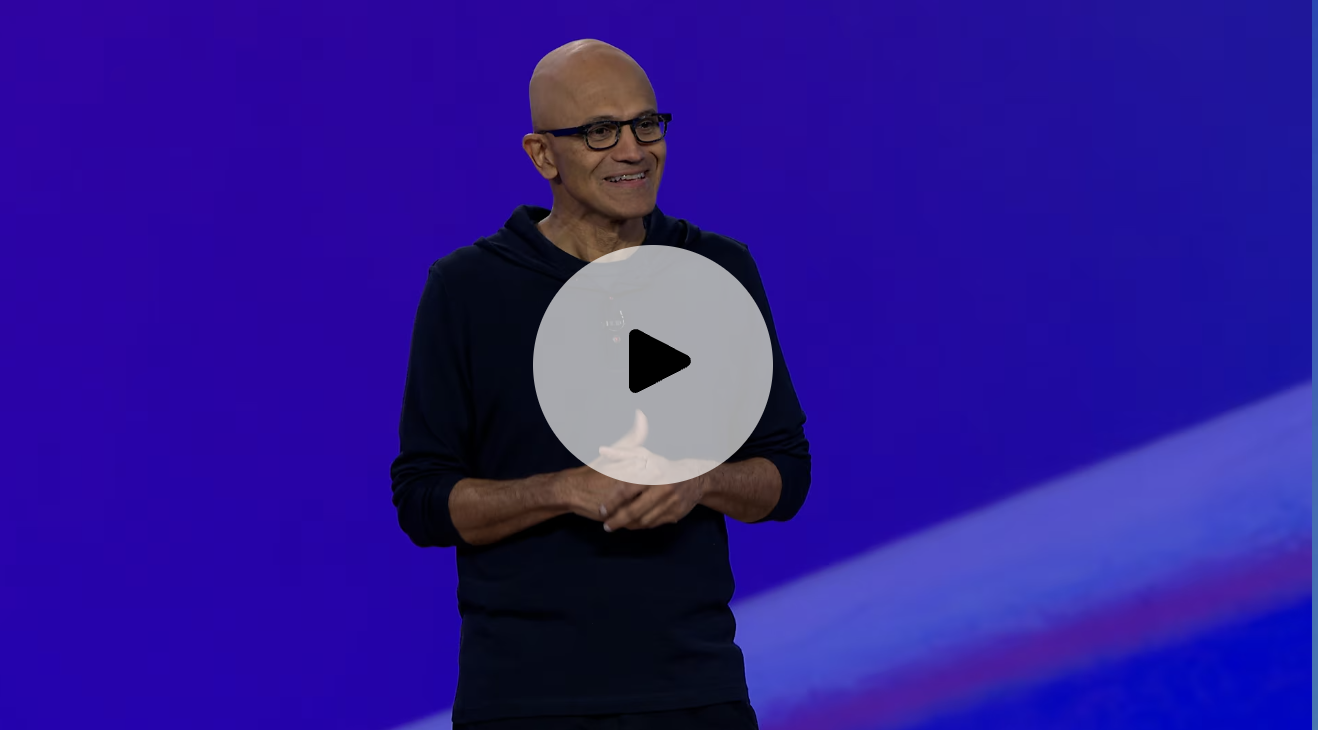 Microsoft CEO, Satya Nadella, stands in front of a blue background. There is a click to play button at the center of the image. 